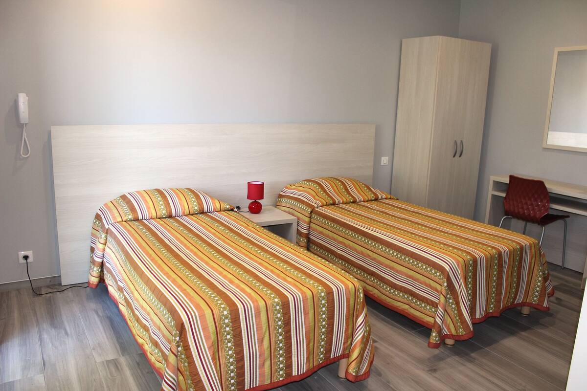 A bedroom with two beds, a wardrobe, a desk, and a chair.