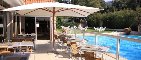 An outdoor pool area with tables and chairs, a covered seating area, and a view of the pool.
