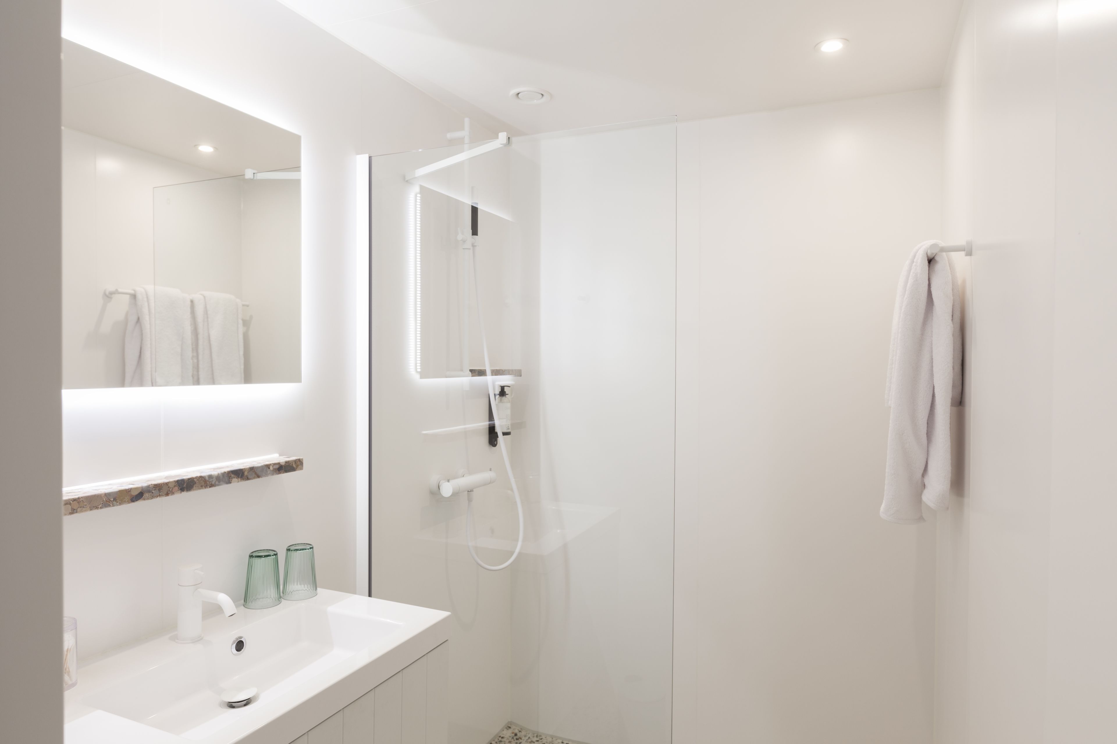 Un baño moderno con un lavabo blanco, cabina de ducha con paredes de vidrio y una toalla colgada en la pared.