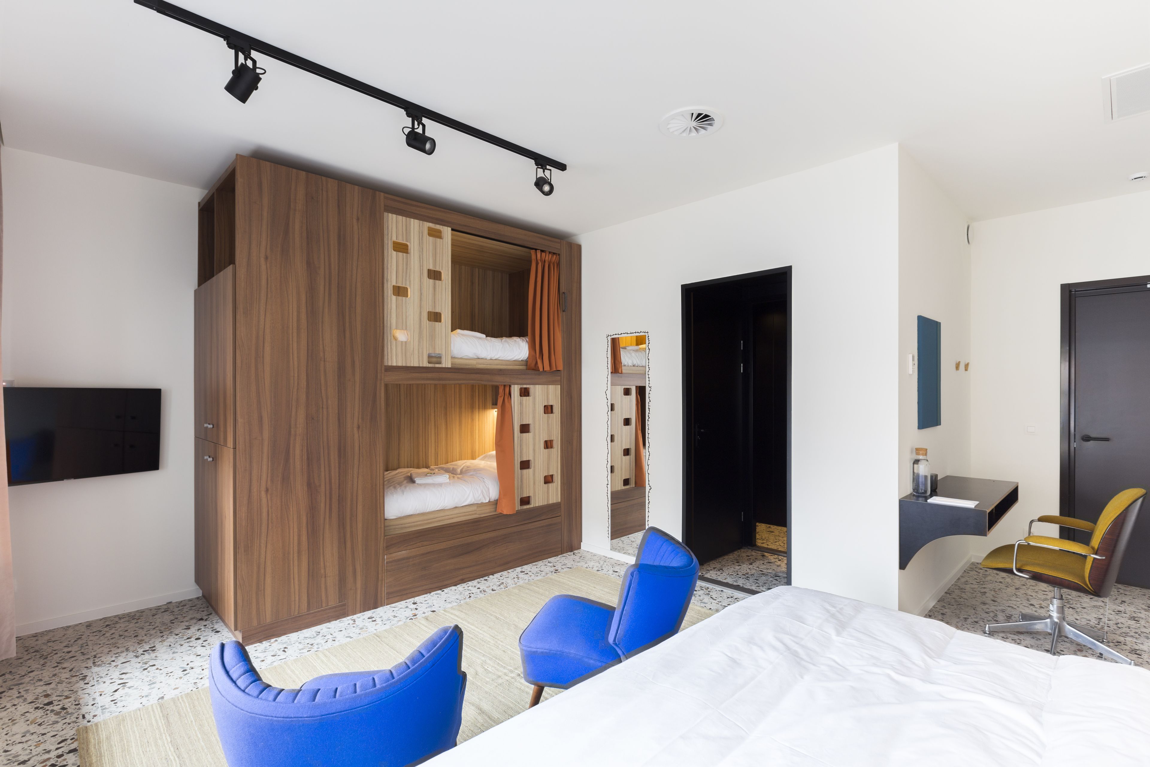 A modern hotel room with a bunk bed, a desk, a chair, and a TV.