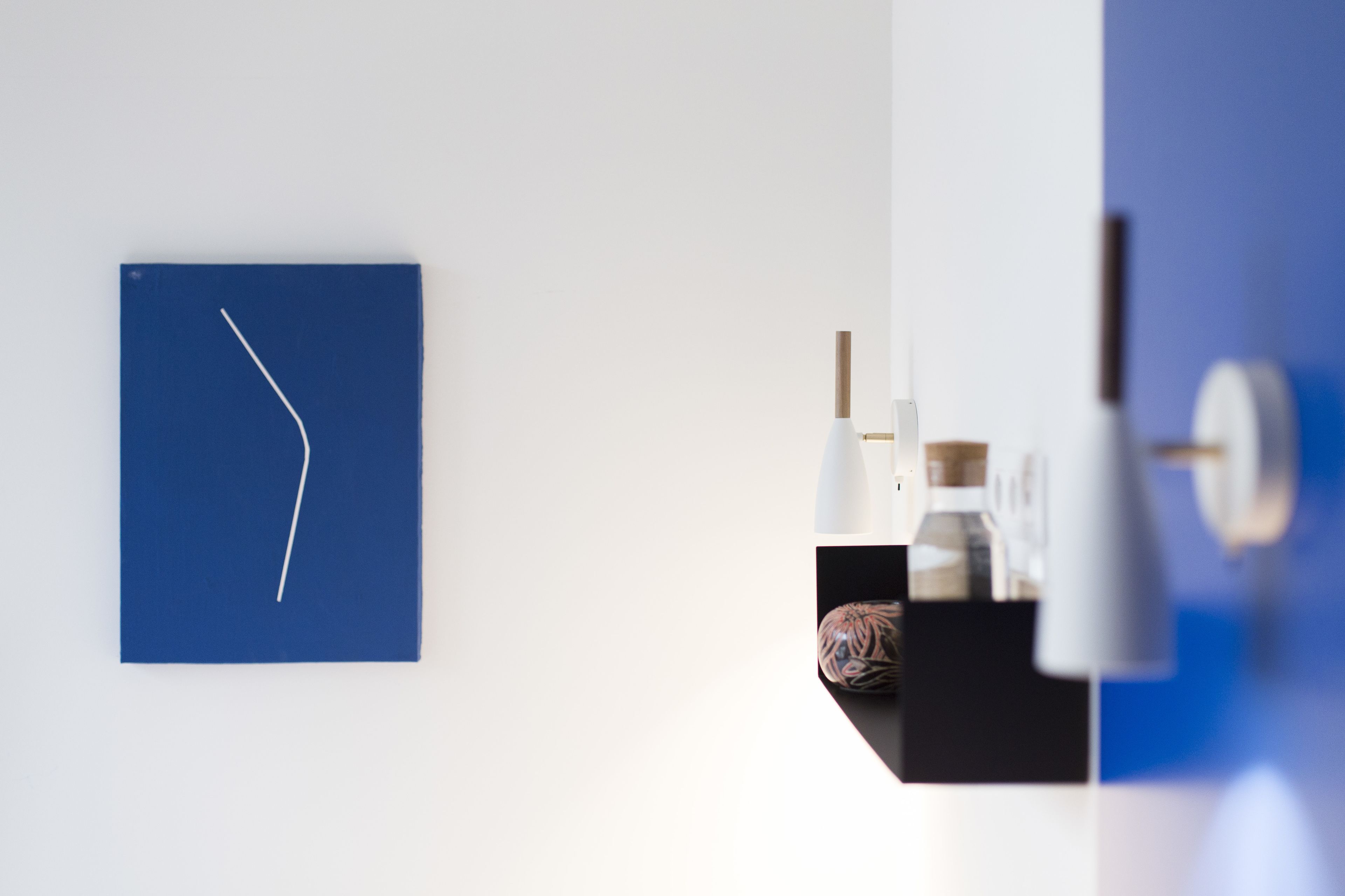 Una habitación moderna con un muro azul de acento, una obra de arte abstracta blanca y un espejo con marco negro que refleja una lámpara blanca y un objeto decorativo.