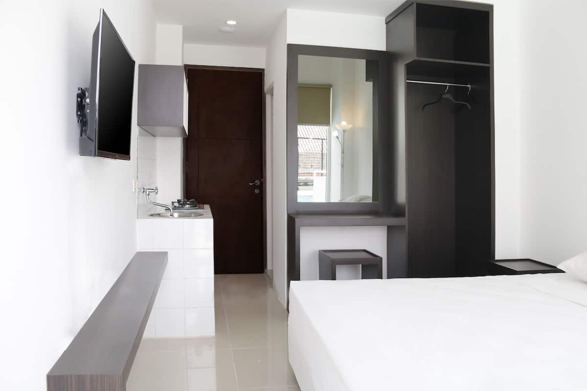 A modern hotel room with a bed, a small desk with a sink, a wardrobe, and a TV mounted on the wall.