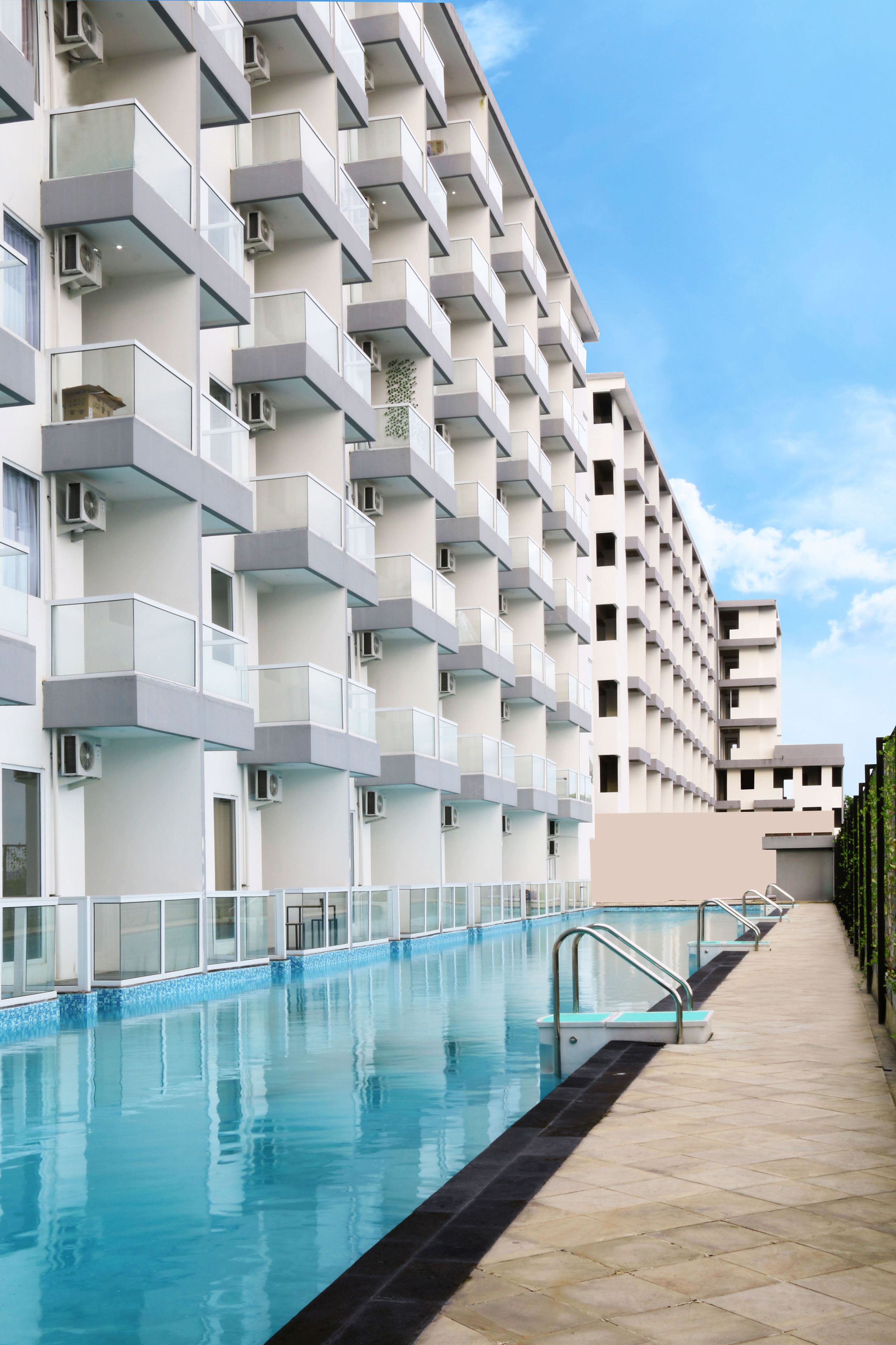Un hotel moderno con piscina, varios balcones y cielo despejado.