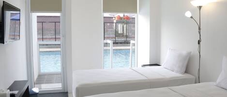 A hotel room with two beds, a TV, and a view of a pool.