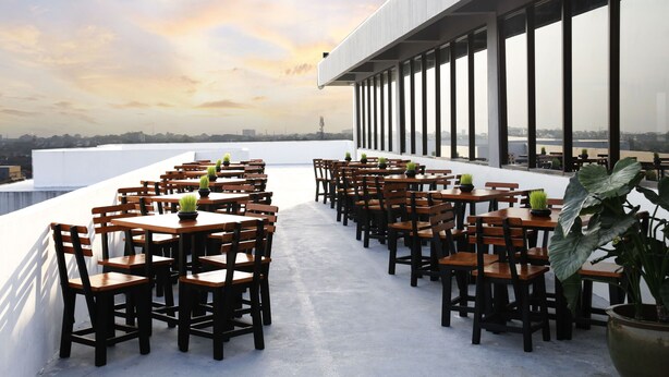A rooftop terrace with wooden tables and chairs, large windows, and potted plants. - Indoluxe Rent Apartment Jogja (Depok)