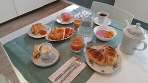 Ein Frühstückstisch mit Croissants, Toast, Marmelade, Orangensaft und einer Teekanne.
