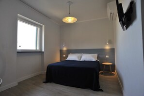 Ein modernes Schlafzimmer mit Bett, Nachttischen, einem Fenster und einer Deckenleuchte.