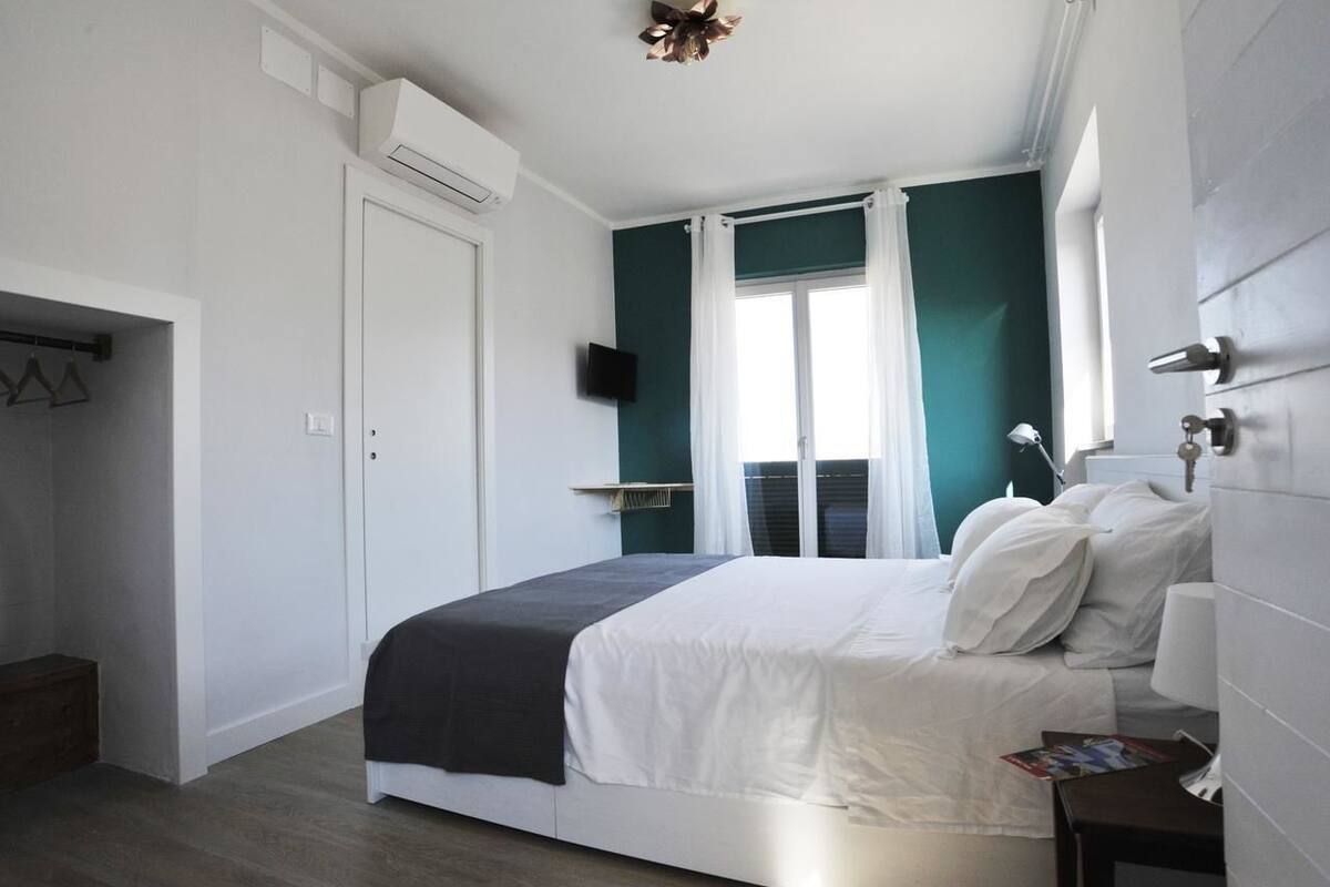 Quarto com cama, televisão, janela com cortinas e porta.