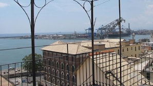 A view from a balcony overlooking a port with industrial cranes, a large ship, and a building with arched windows. - Aquarium Rooms (Genoa)