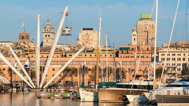 A marina with boats docked, a large white crane structure, and historic buildings in the background. - Aquarium Rooms (Genoa)