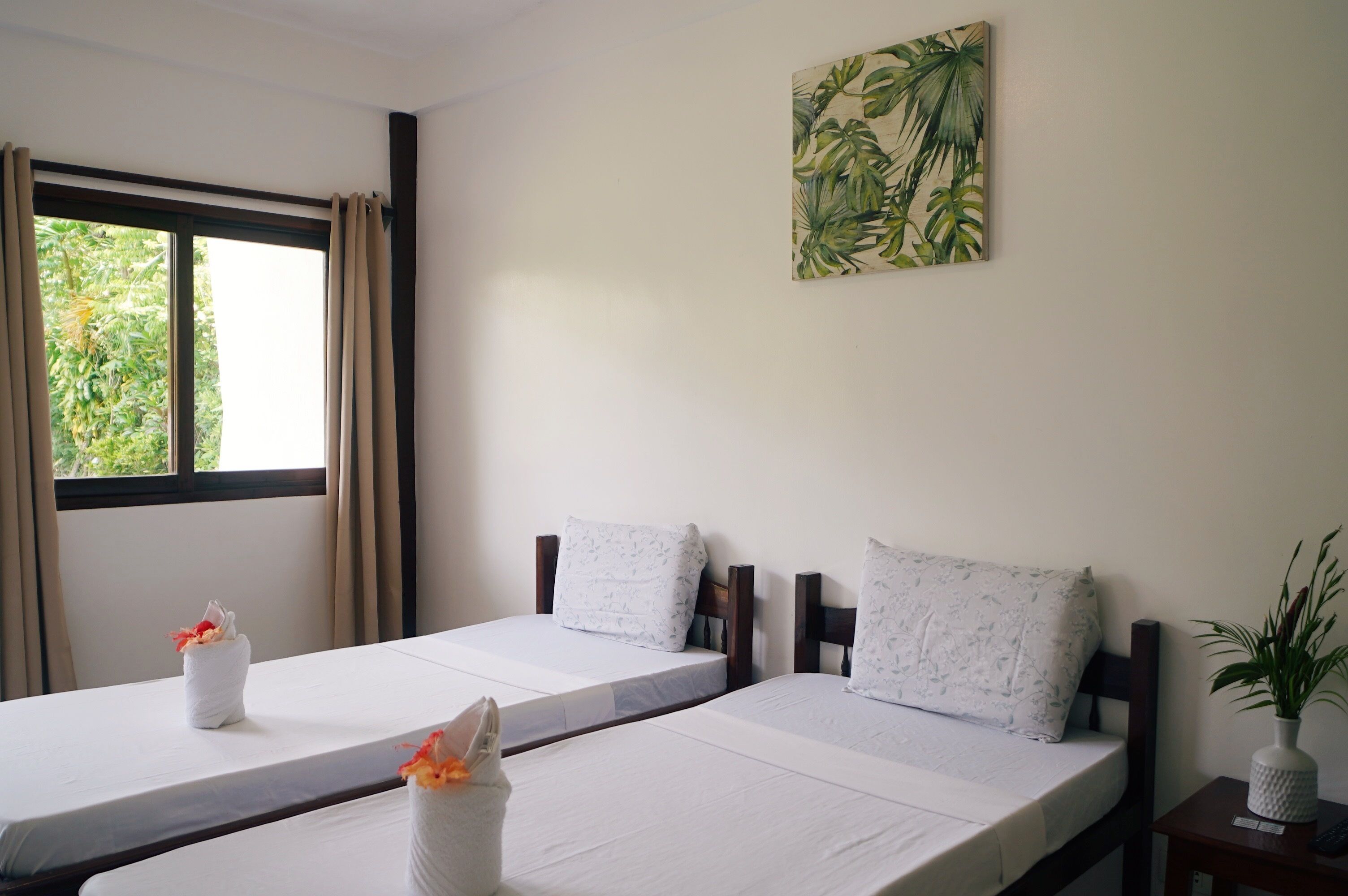 Una habitación de hotel con dos camas, una ventana con cortinas, un cuadro en la pared y una mesita con una planta.