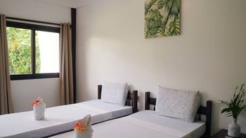 Una habitación de hotel con dos camas, una ventana con cortinas, un cuadro en la pared y una mesita con una planta.