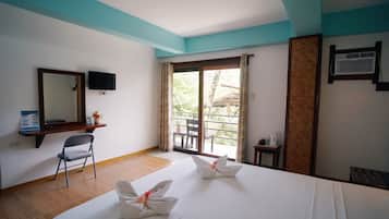 Habitación de hotel con una cama, una silla, televisión, ventana con cortinas y una mesita con hervidor.