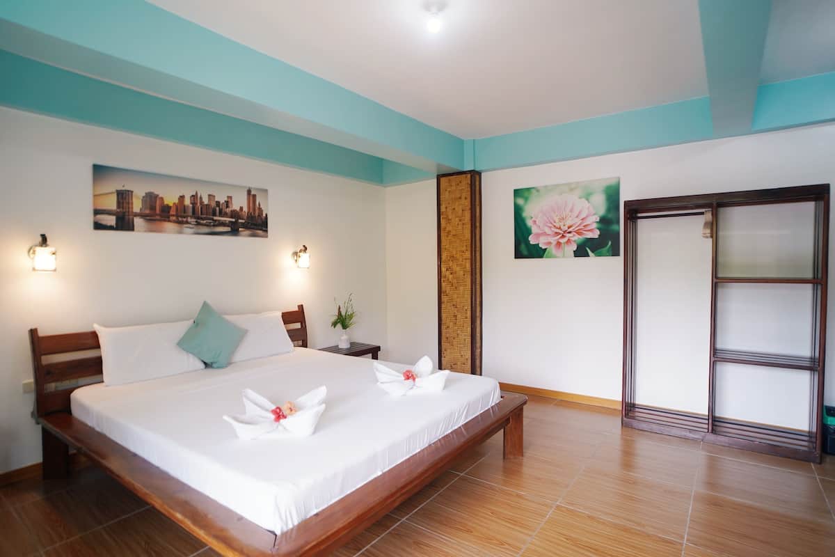 Une chambre d’hôtel avec un grand lit, un tableau représentant un paysage urbain, un tableau représentant des fleurs et une porte coulissante.