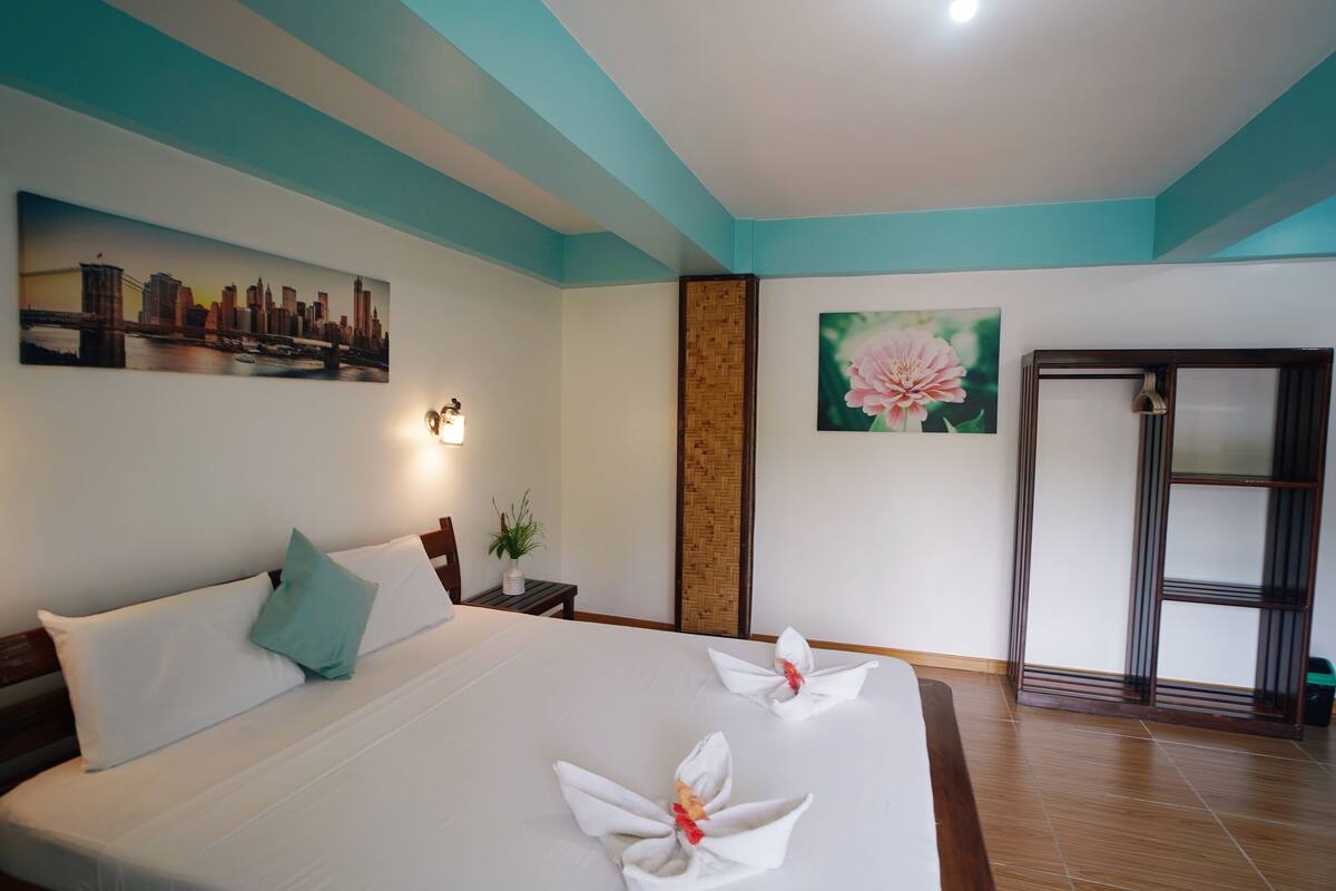 Une chambre d’hôtel avec un grand lit, un tableau représentant un paysage urbain, une œuvre d’art florale, un mur décoratif en bois et une porte coulissante.