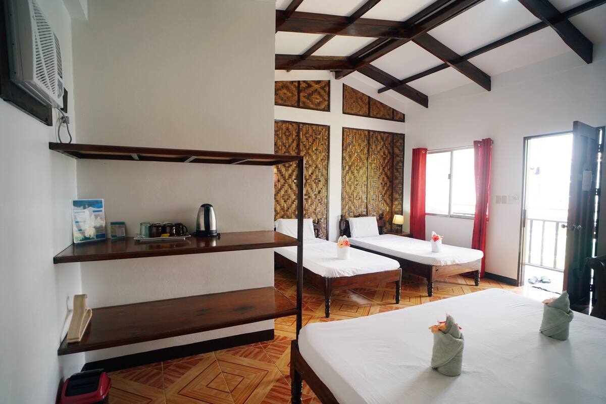 Une chambre d’hôtel avec deux lits, un plancher en bois, une étagère avec des articles de toilette et une fenêtre avec des rideaux.