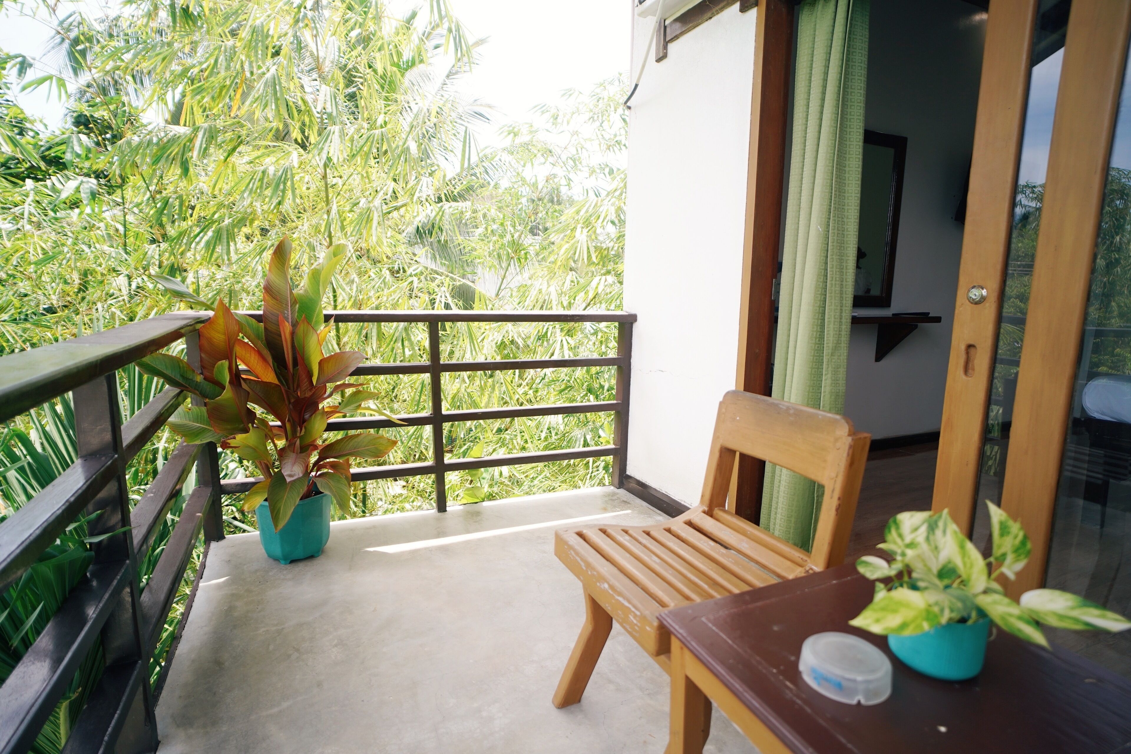 Een balkon met een houten stoel en tafel, omringd door potplanten en uitzicht op weelderige begroeiing.