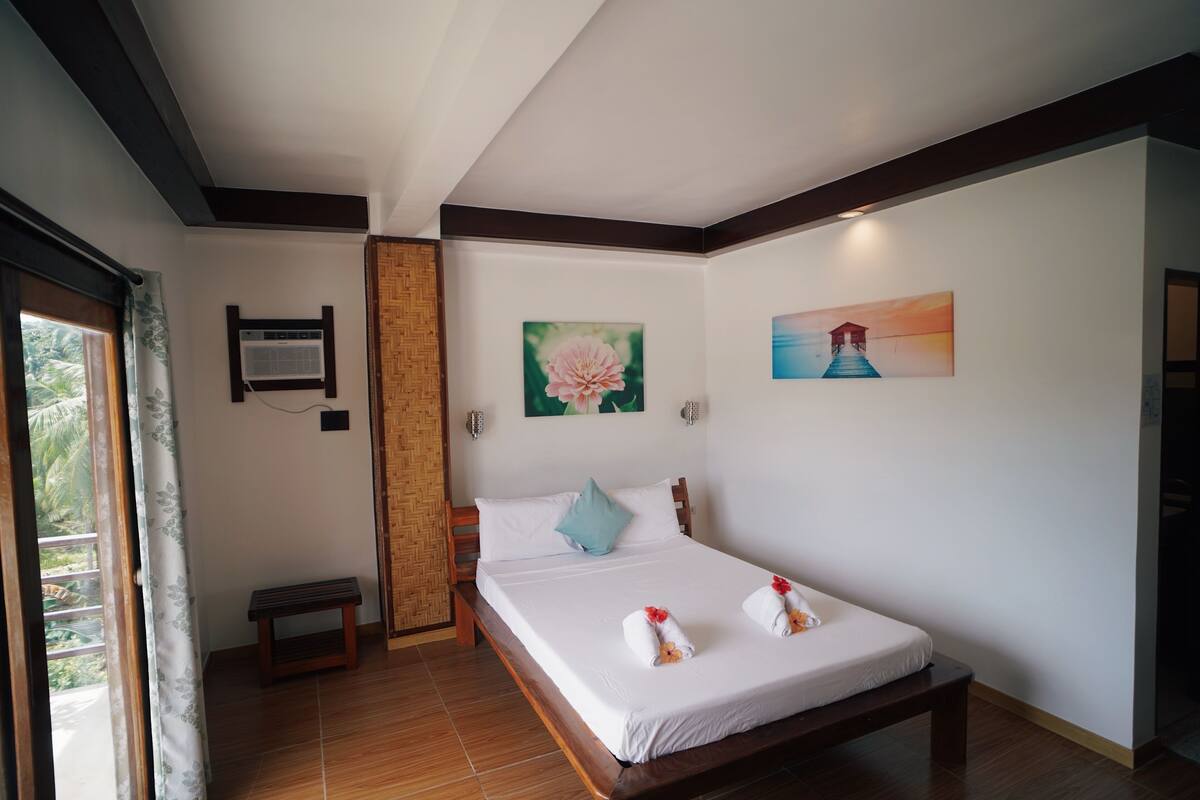 Une chambre bien rangée, avec un lit, des oreillers, un banc et des œuvres d’art accrochées aux murs.