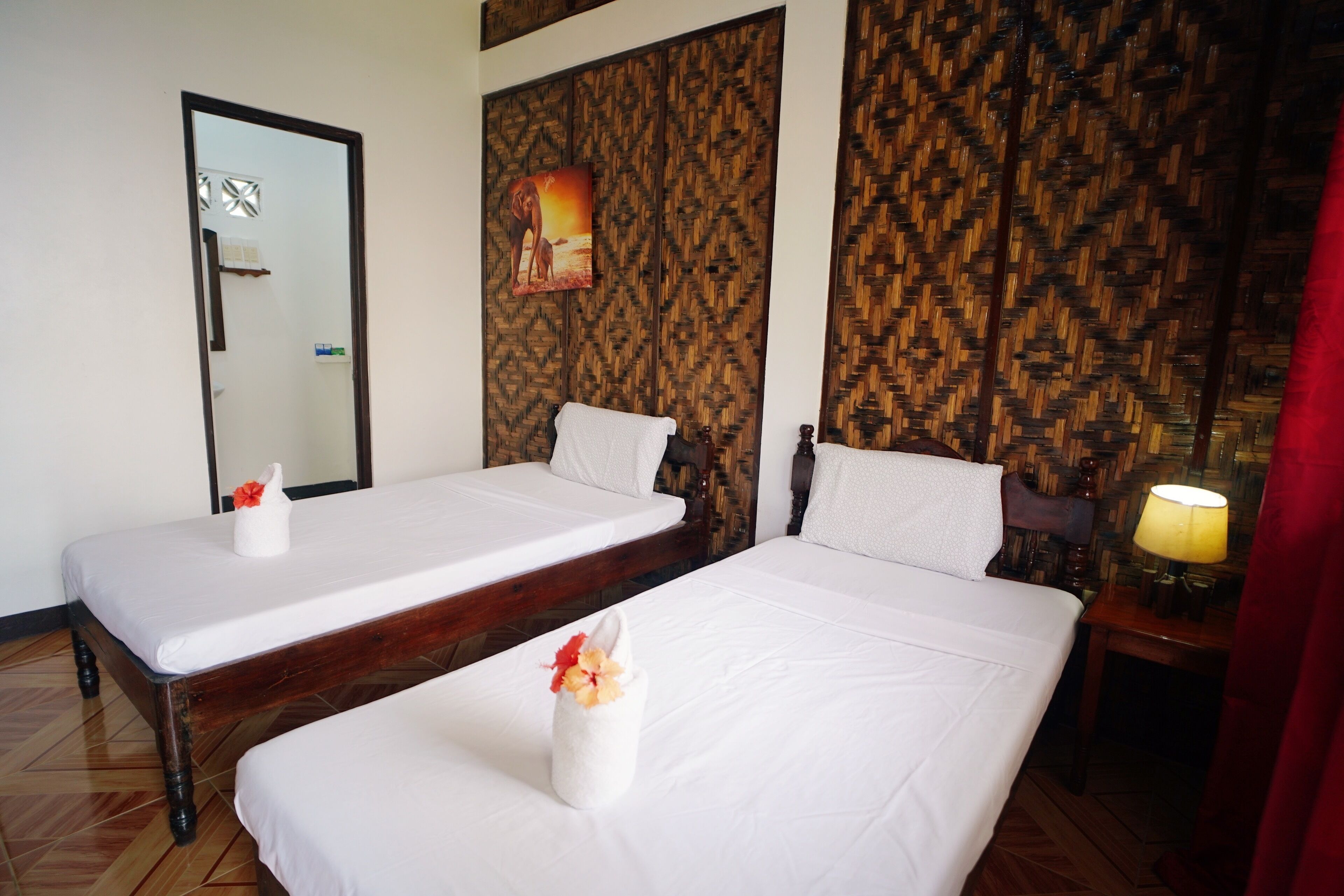 Ein Hotelzimmer mit zwei Einzelbetten, einem Holz-Kopfteil, einem Spiegel, einer Wand mit Webmuster und einem Gemälde.