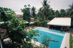 Una piscina rodeada de exuberante vegetación y palmeras, con una zona cubierta y sillas de descanso.