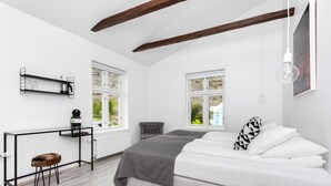 Un dormitorio moderno con una cama, un escritorio y una silla. Hay dos ventanas y un radiador.