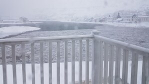 Escena nevada de un río con una baranda blanca al frente.