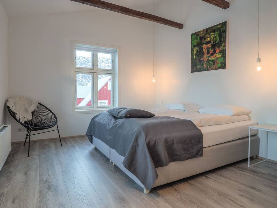 Een slaapkamer met een bed, een stoel, een raam en een schilderij.