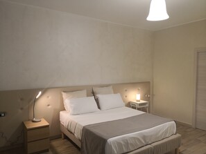 Um quarto com cama, mesas de cabeceira, luminária e apoio para objetos pessoais.