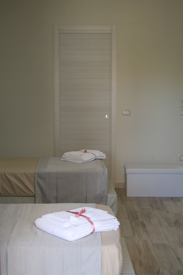 A hotel room with a bed, a small table with folded towels, a bench, and a toilet.