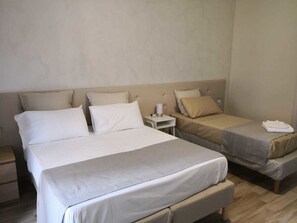 Quarto de hotel com duas camas de solteiro, uma cama grande e uma mesa de cabeceira com abajur.