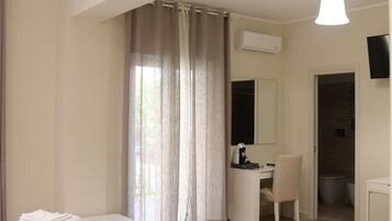 Habitación de hotel con cama, escritorio, silla, unidad de aire acondicionado y televisor.