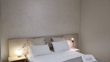 Une chambre d’hôtel comprenant un lit, deux tables de chevet, une petite table et une lampe fixée au mur.