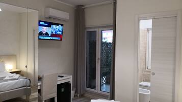 A hotel room with a bed, desk, chair, TV, and a view of the outside.