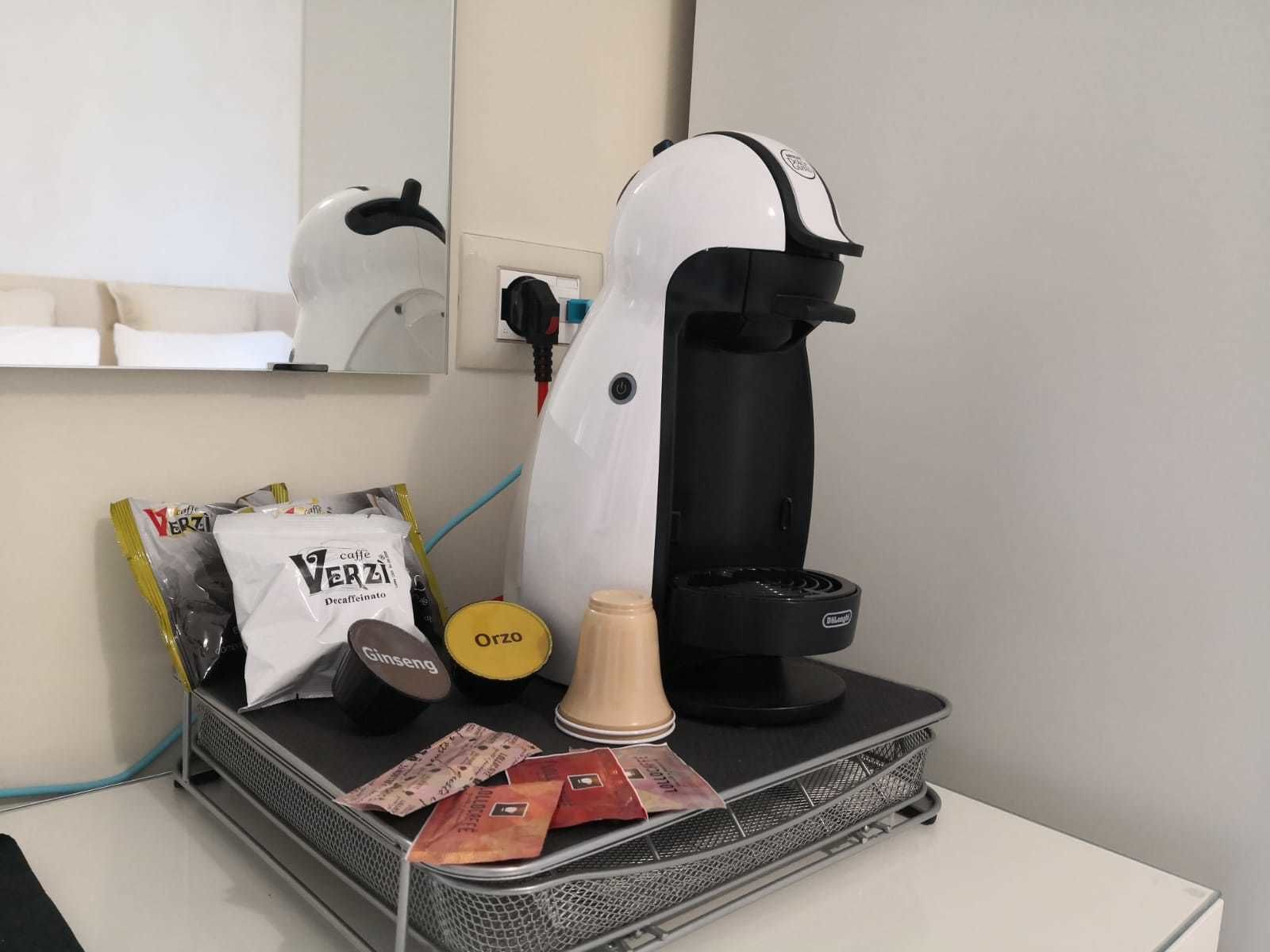 A coffee machine, a bag of Verza decaffeinated coffee, a Ginseng packet, a yellow cup, and some coffee packets on a metal tray.