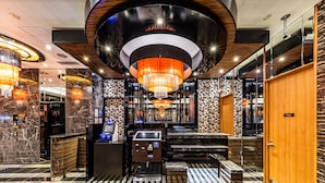 Een moderne lobby met een grote kroonluchter, marmeren wanden en een receptiebalie met een zelfbedieningskiosk.