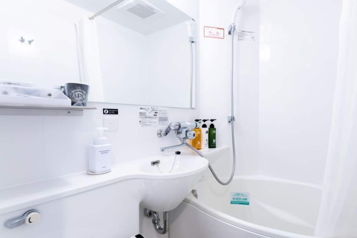 A bathroom with a sink, mirror, shower, and a bottle of hand soap.