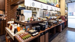 Een buffetopstelling met diverse gerechten en drankjes, een koffieapparaat en een groot raam met uitzicht op een groen landschap.