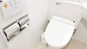 A modern bathroom with a toilet, a paper towel dispenser, and a hand dryer.