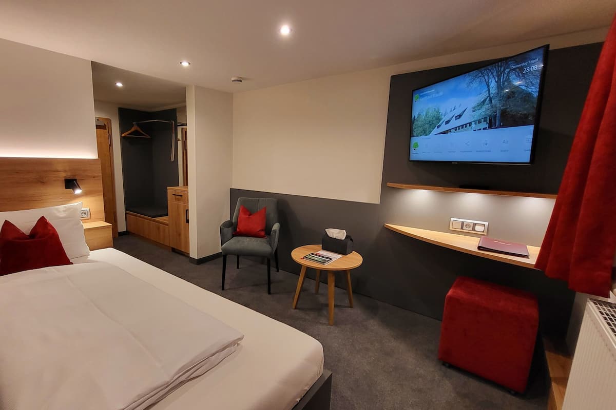 A hotel room with a bed, a desk, a chair, a TV, and a red curtain.