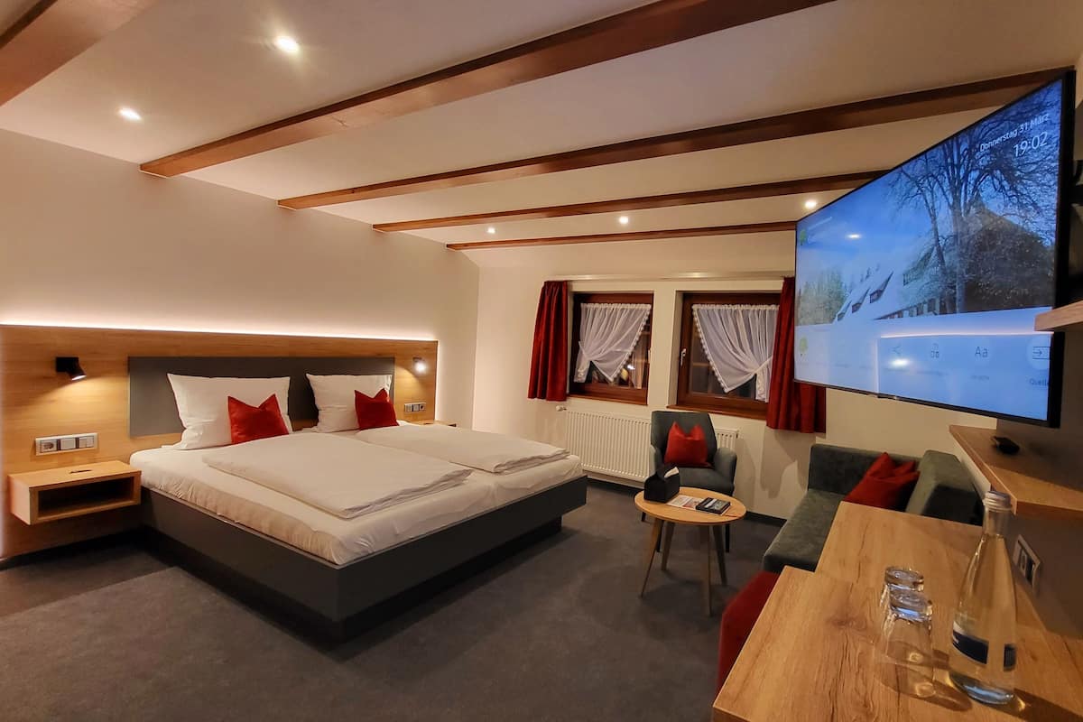 A modern hotel room with a large bed, a TV, a desk, and a chair.