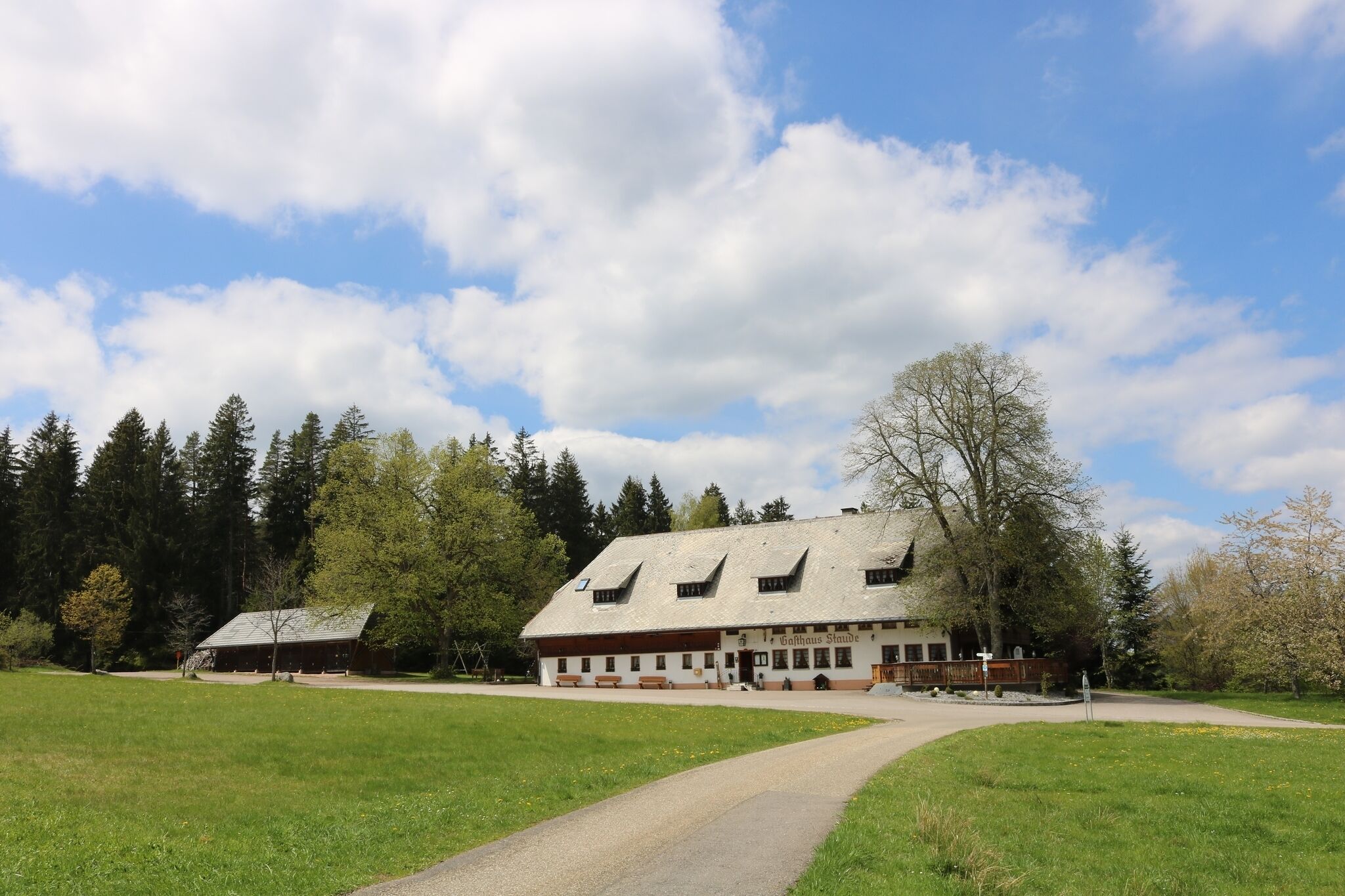 A traditional chalet-style building with a sloped roof, surrounded by a grassy field and trees.