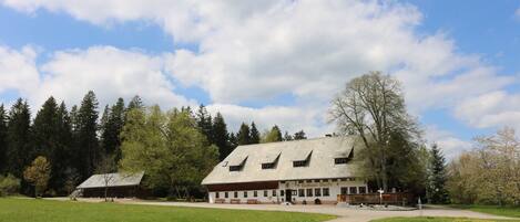 A traditional chalet-style building with a sloped roof, surrounded by a grassy field and trees.