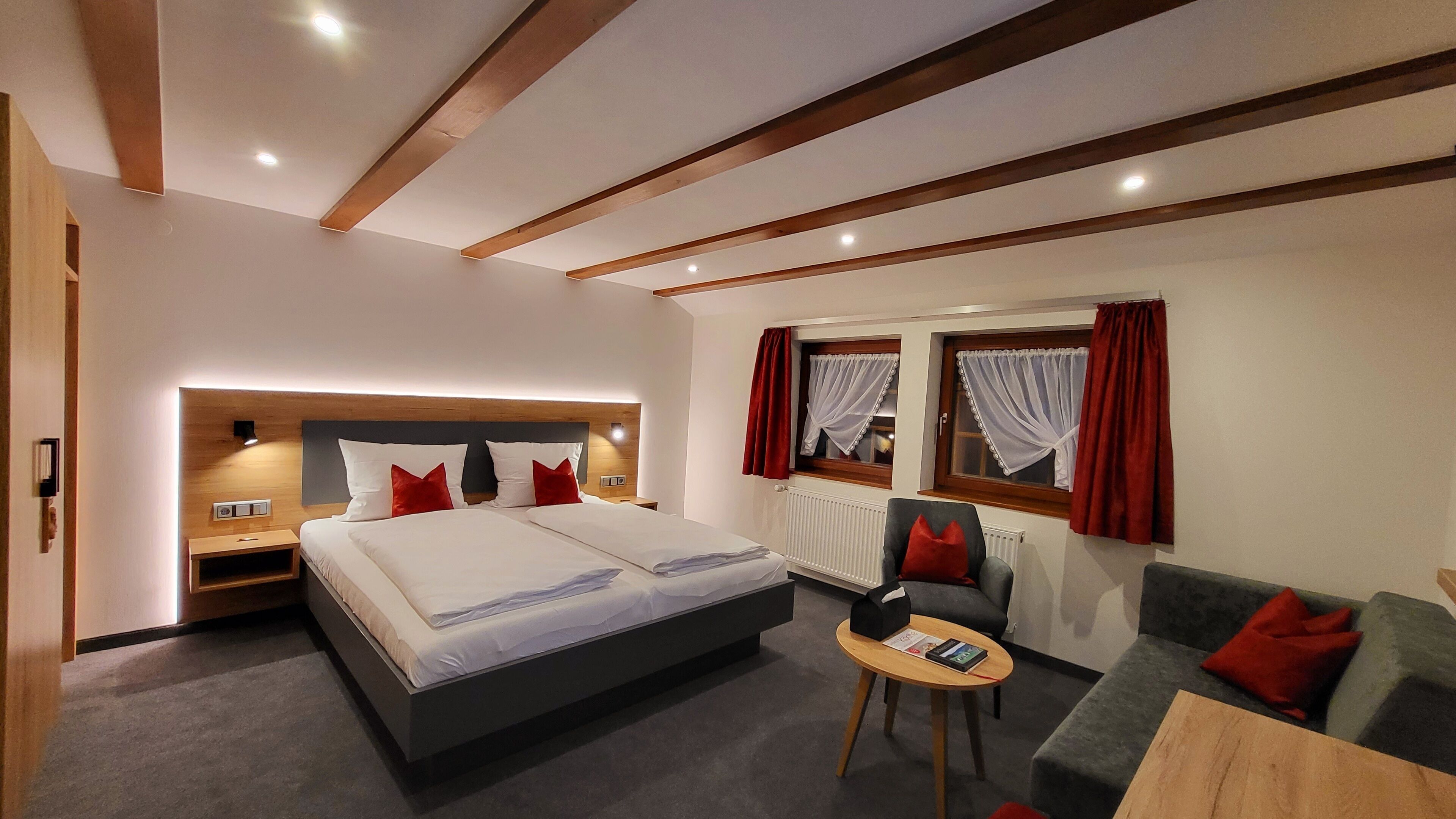 Een hotelkamer met een groot bed, een kleine zithoek, een tafel en een raam met gordijnen.
