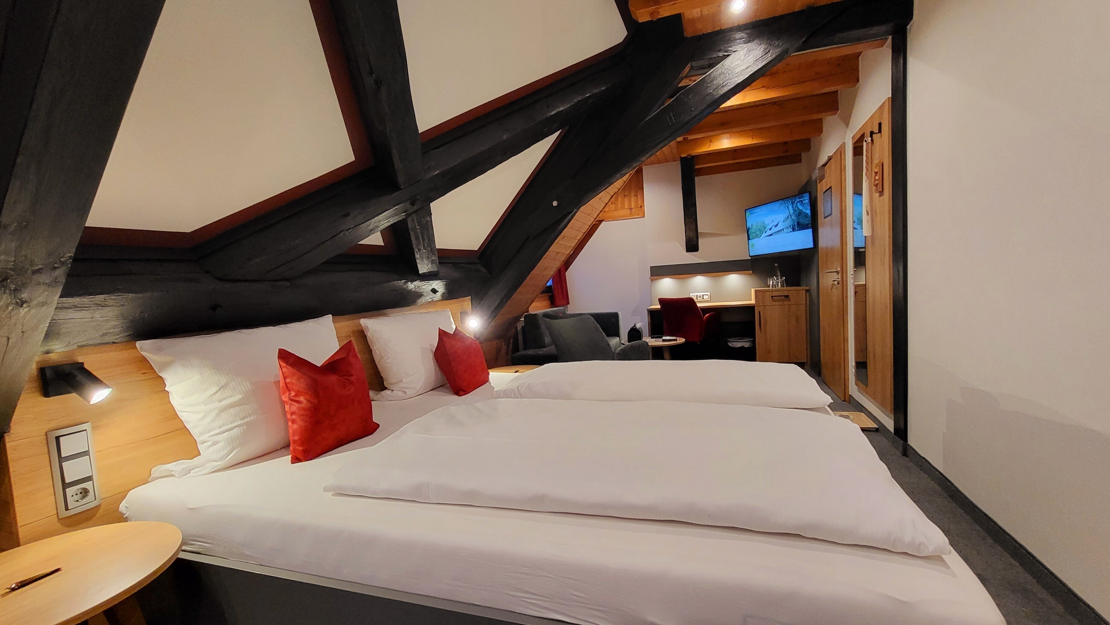 A hotel room with a large bed, a desk, a chair, and a television.