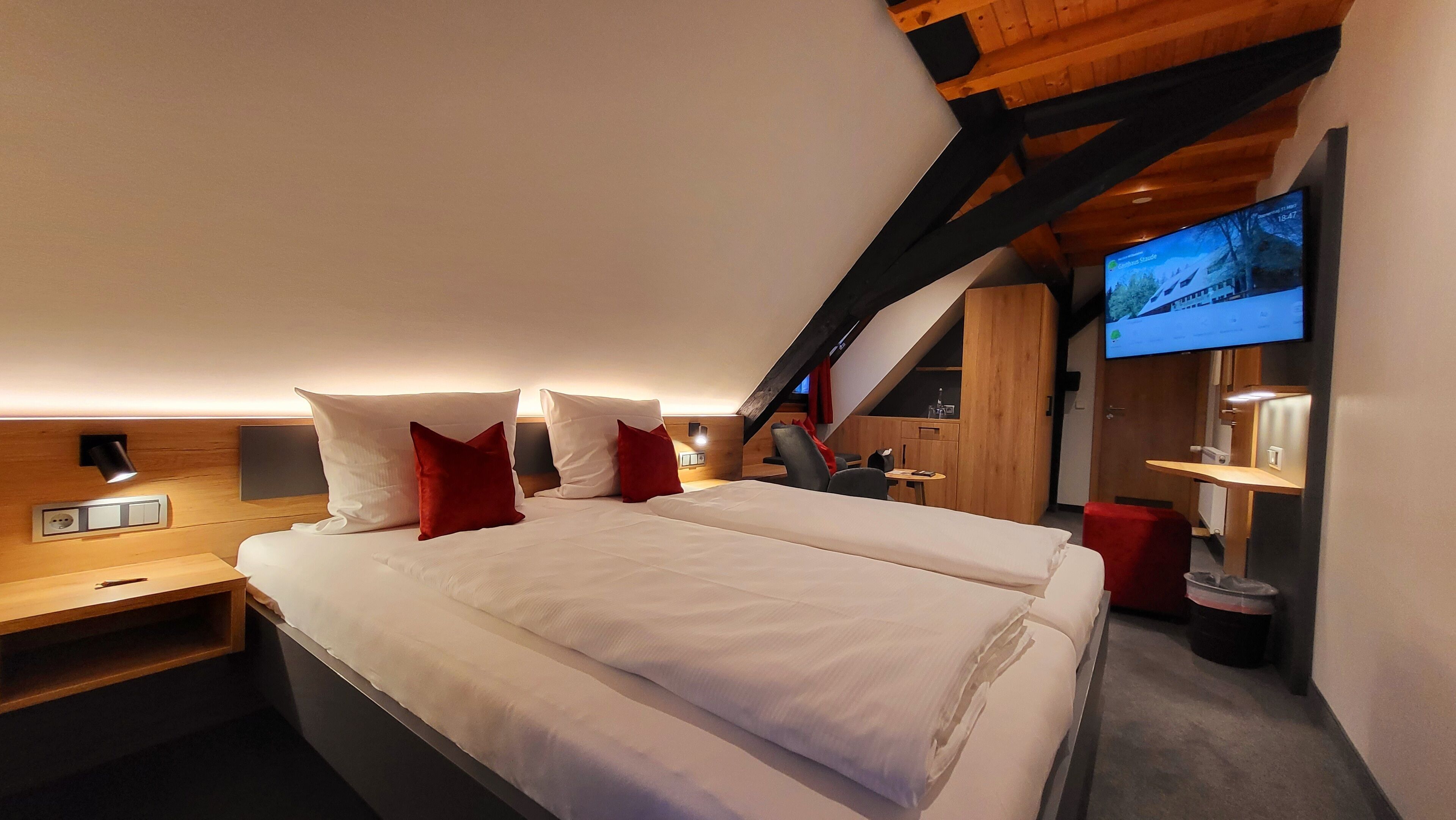 A modern bedroom with a large bed, wooden headboard, and a TV mounted on the wall.