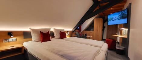 A modern bedroom with a large bed, wooden headboard, and a TV mounted on the wall.
