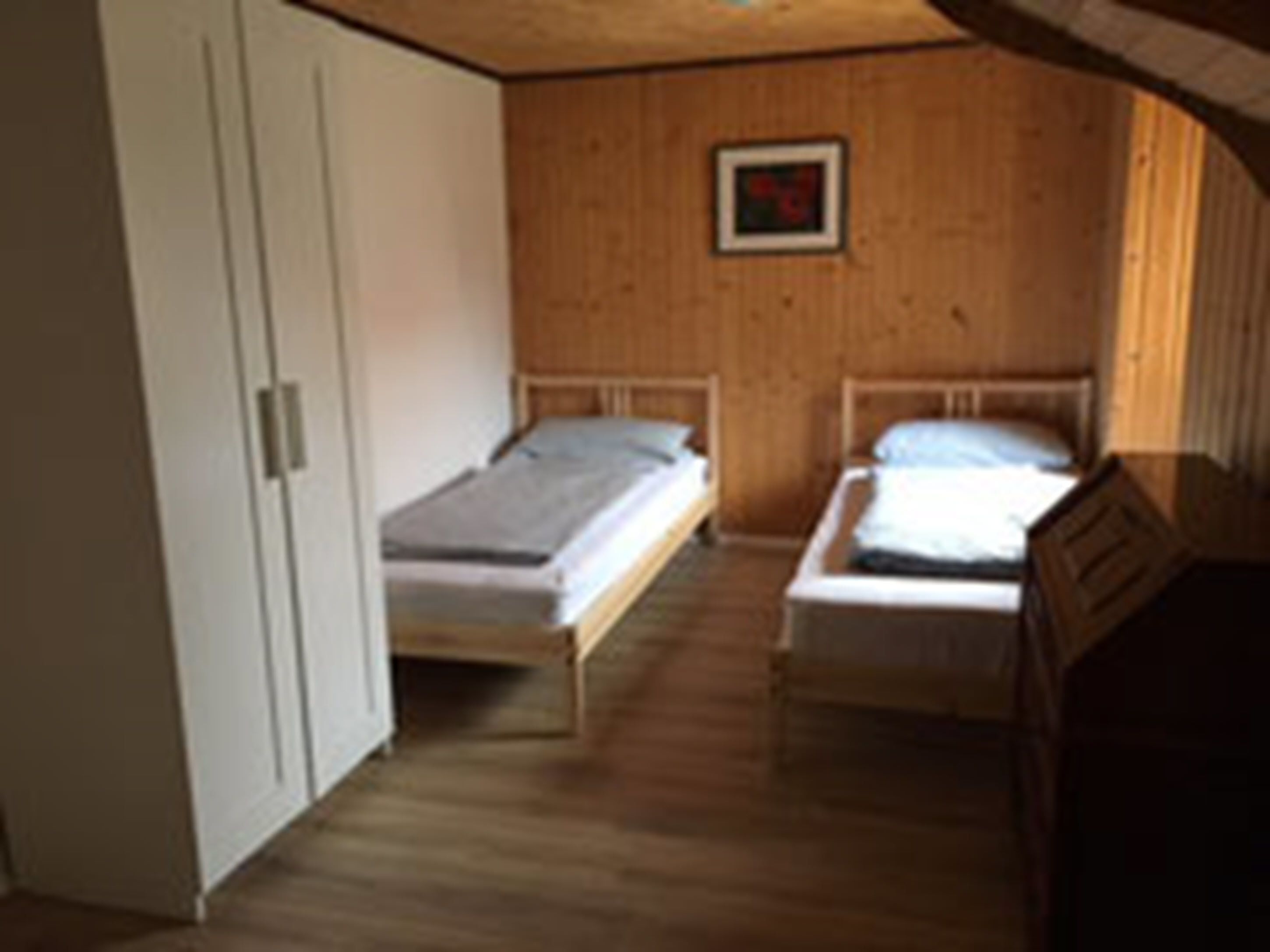 Una habitación pequeña y acogedora con dos camas individuales, paredes de madera y un armario blanco.