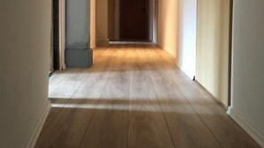 A hallway with wooden flooring, a wooden ceiling, and a door on the right.
