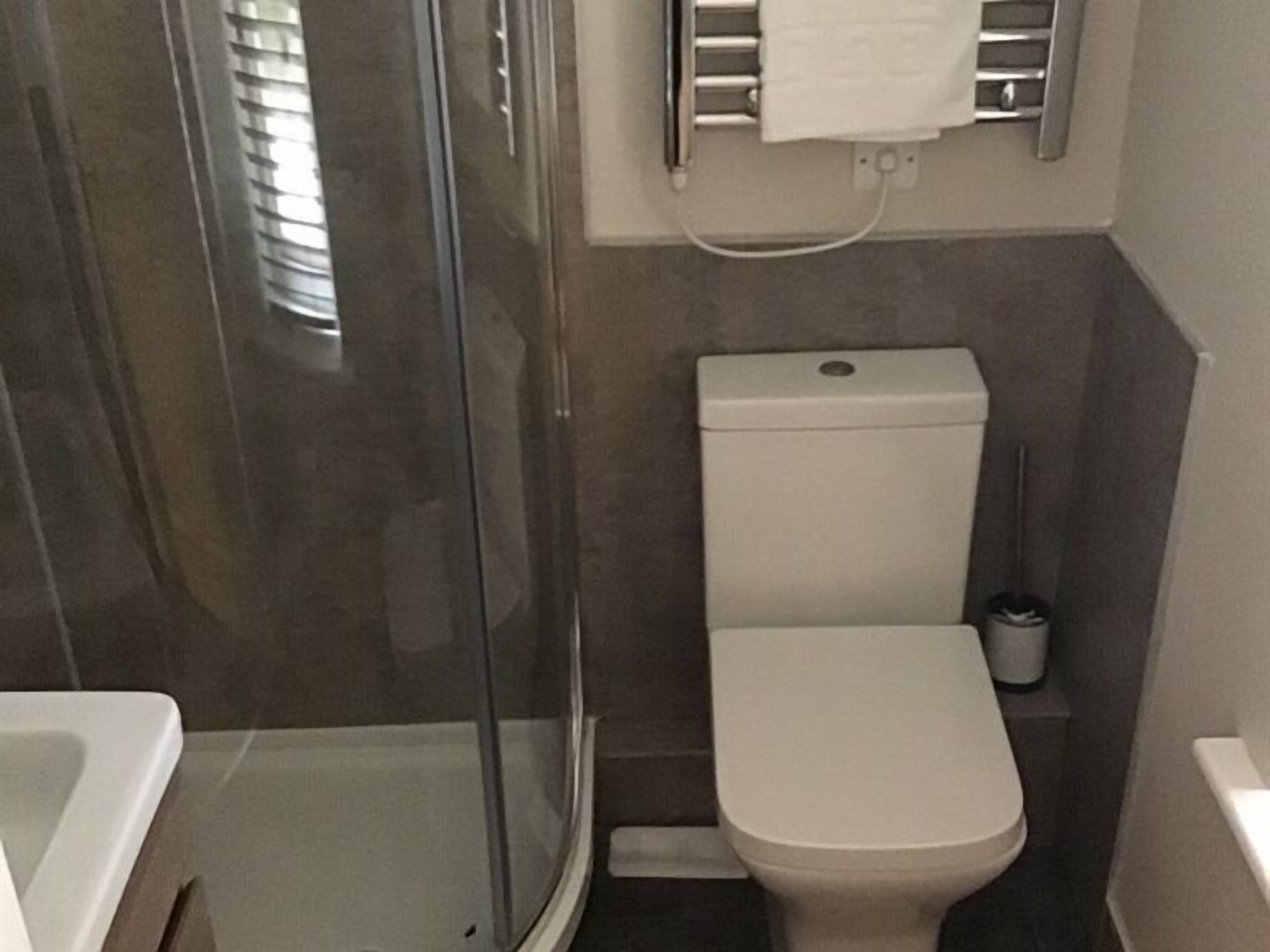 A small bathroom with a glass shower enclosure, a toilet, and a towel rack.
