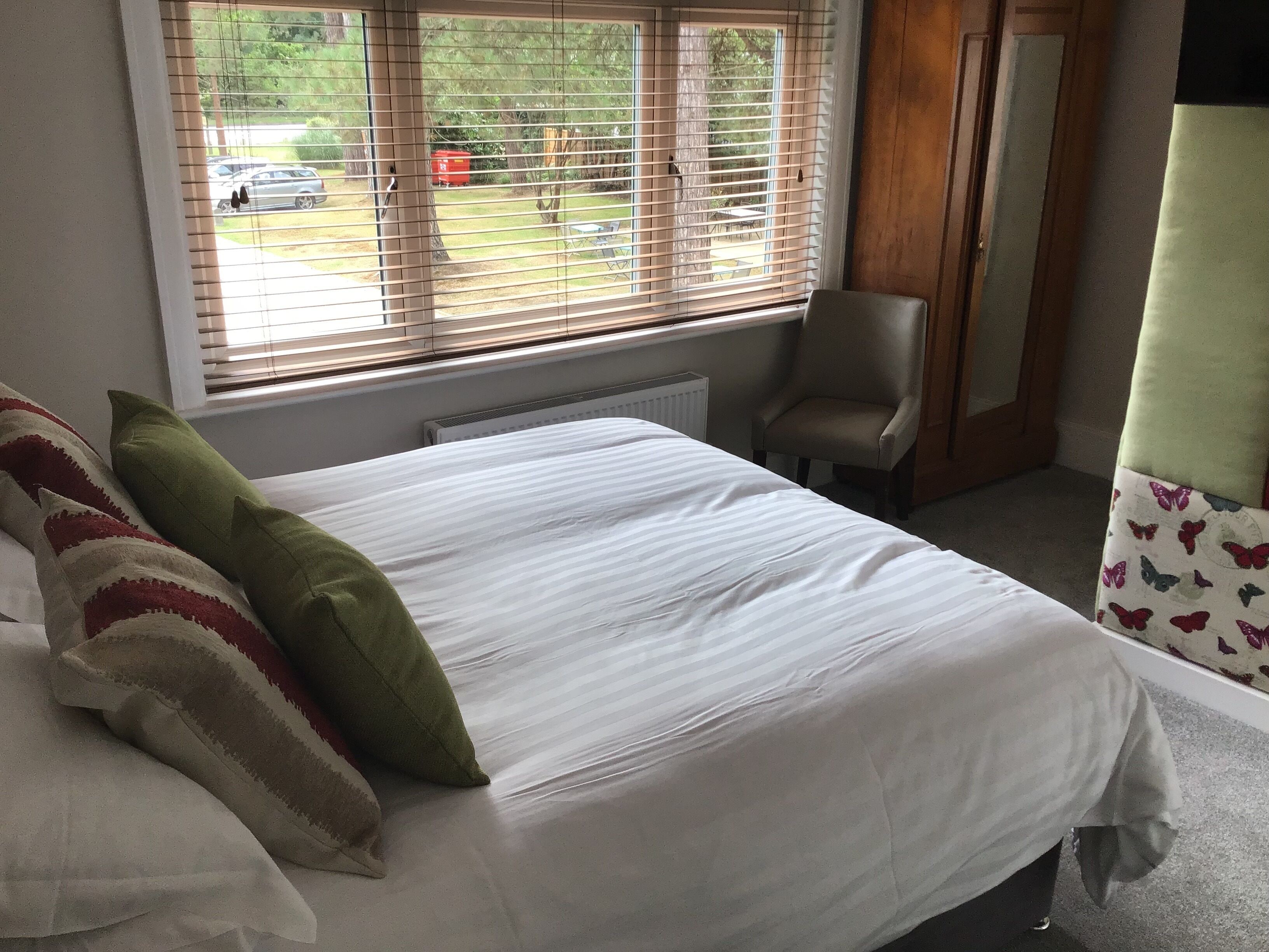 A bedroom with a large bed, a chair, and a window with blinds.